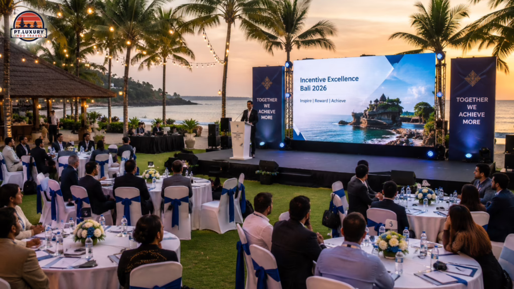 Outdoor corporate event on a Bali beach at sunset with a speaker and a screen reading Incentive Excellence Bali 2026